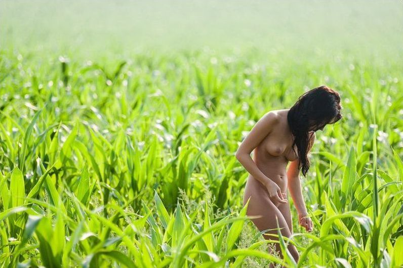 young red haired girl undresses her white sleeveless shirt on the green field outside in the nature