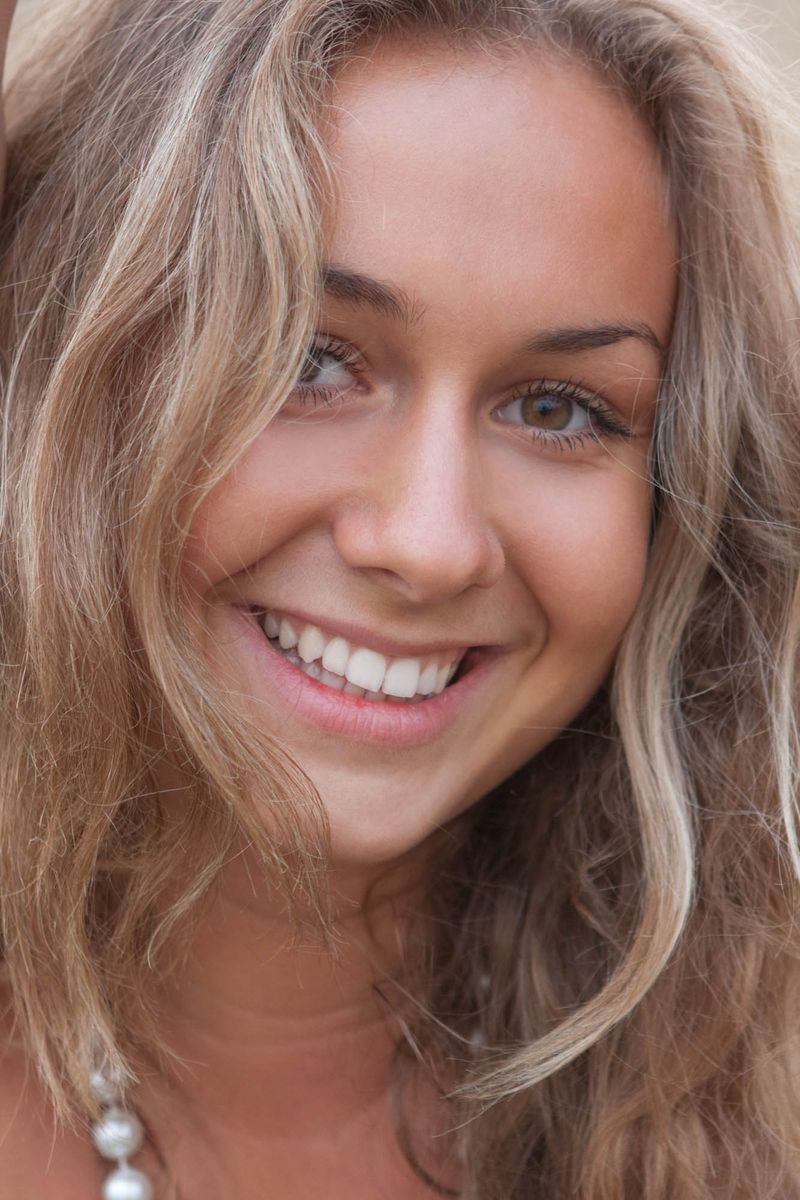 curly blonde girl with a white pearl necklace reveals outside on the glade field at the tree