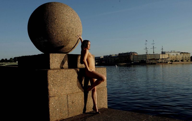 young brunette girl reveals her coat at the rostral column lighthouse in the city of saint petersburg