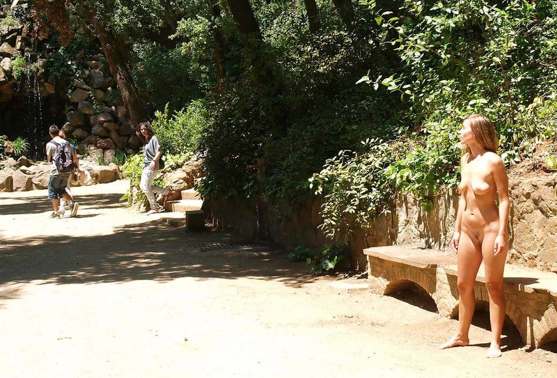 young brunette girl naturist posing nude on the walking trail in the public park with small cascade waterfalls