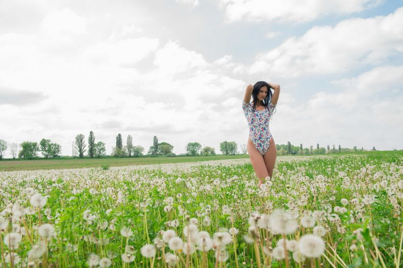 young black haired girl undresses her bodysuit on the field of dandelions