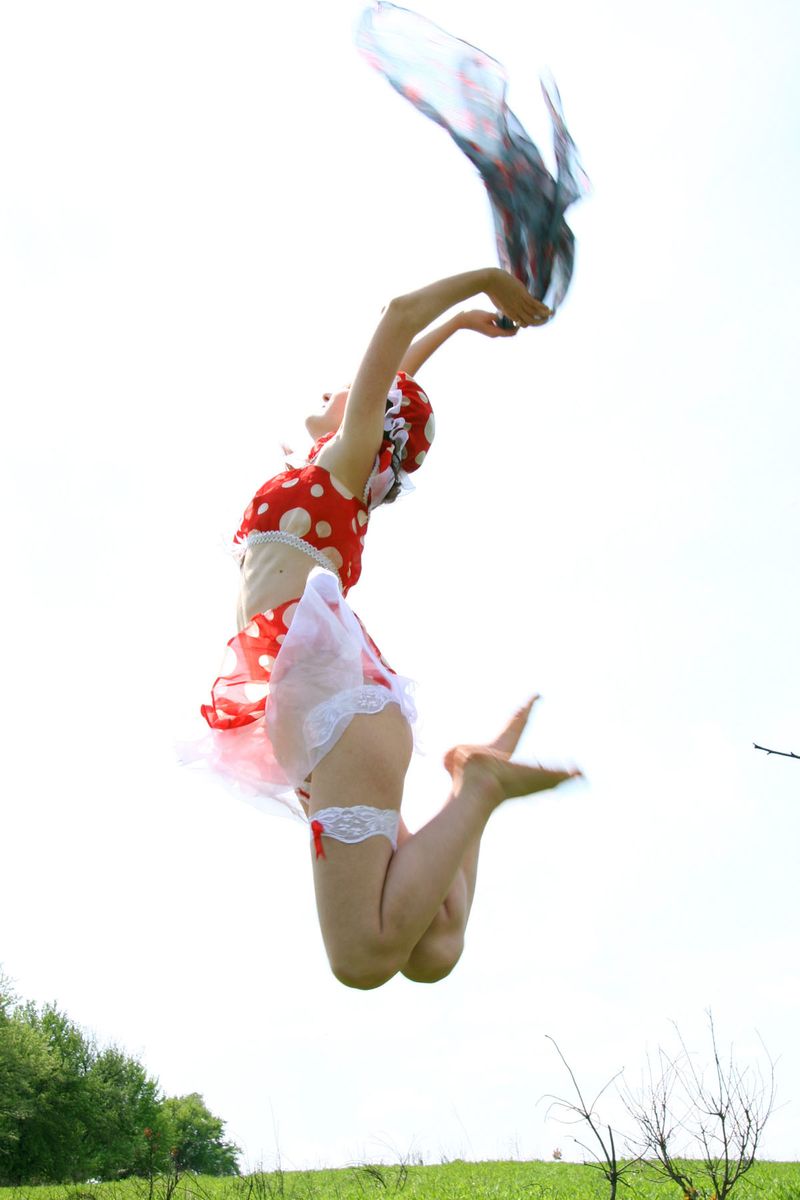 young red haired girl reveals her red and white dress with white panties outside on the grassy glade meadow