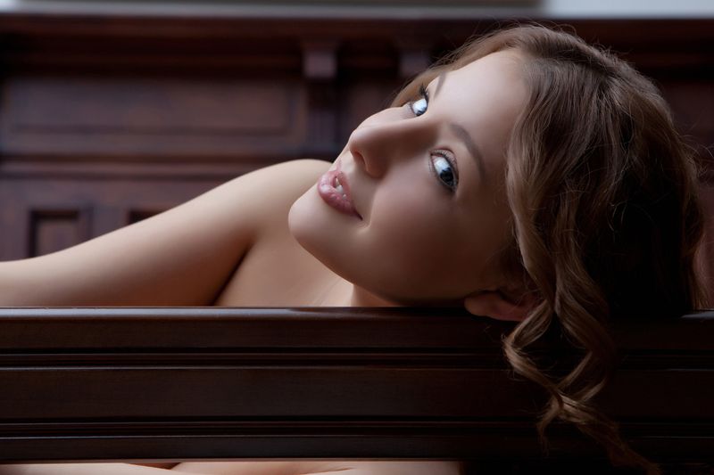 cute young curly dark blonde girl with blue eyes posing in the room with a bed and vanity table with the mirror