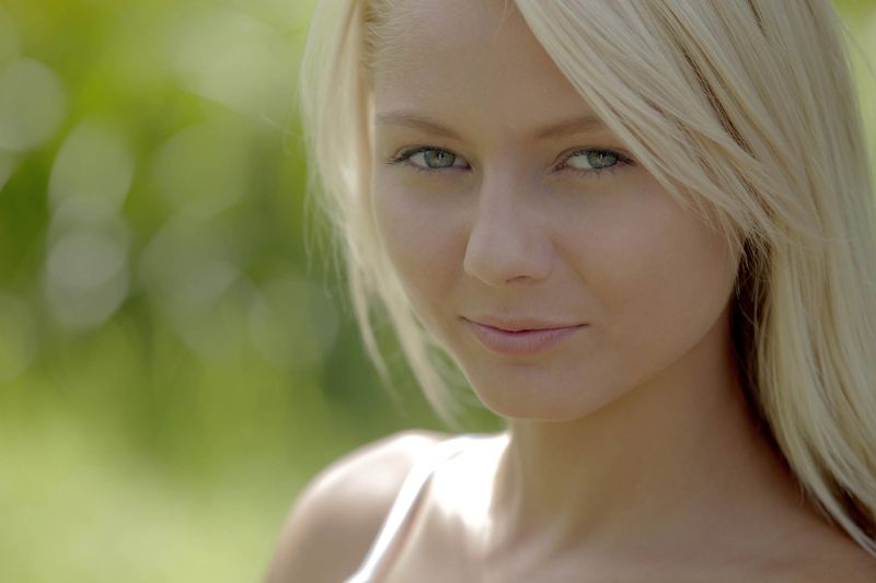 cute young blonde girl with blue eyes reveals her white camisole and jean skirt outside on the small wooden bridge