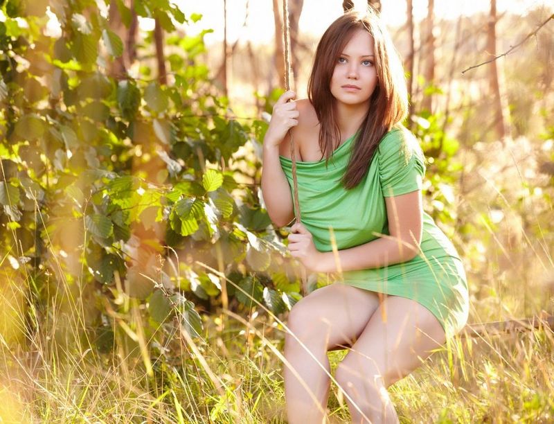 cute young brunette girl with blue eyes and full natural breasts strips her green dress outside on the wooden swing