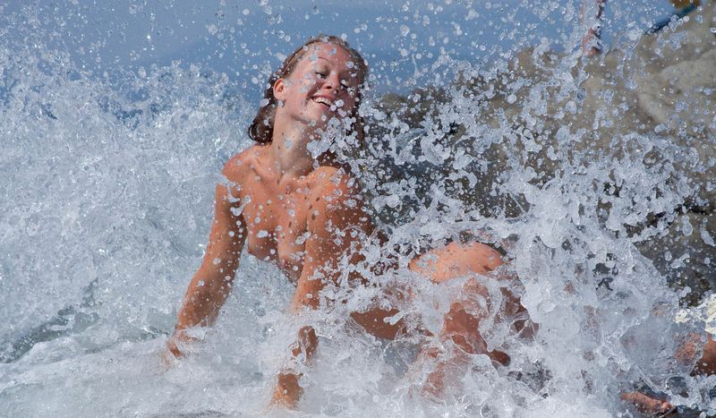 young blonde girl undresses her white blouse on the rocky shore at the sea