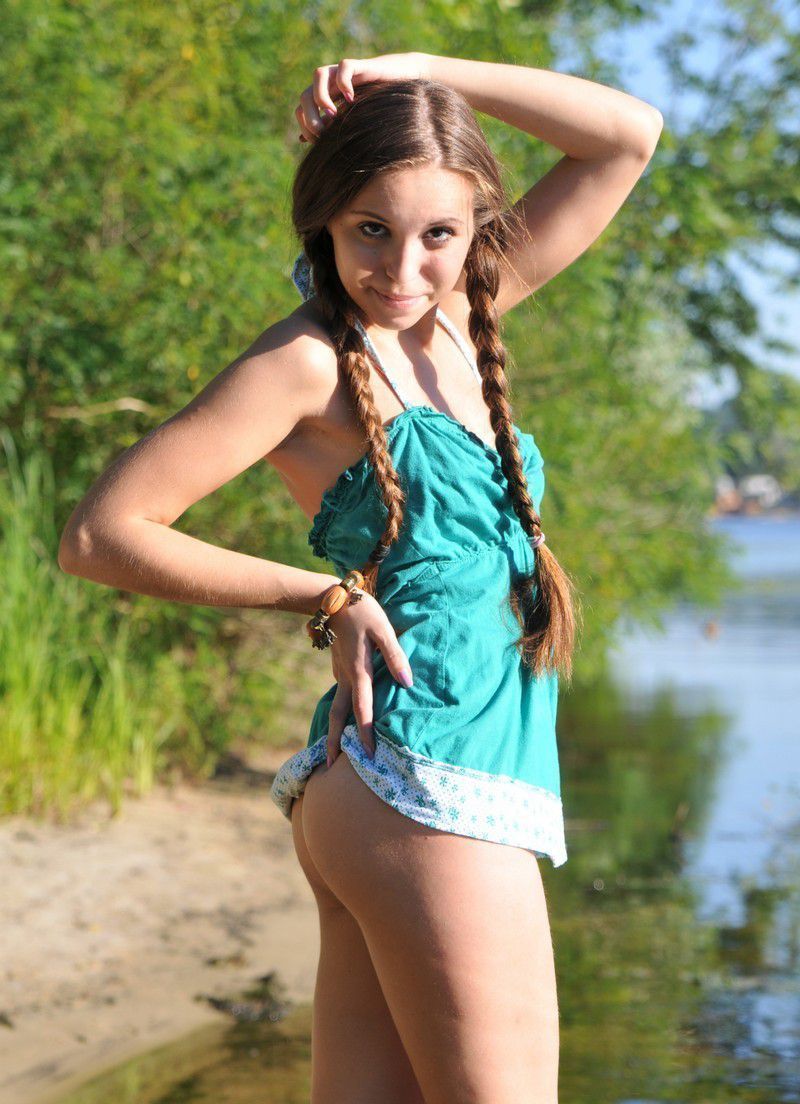 young brunette girl with pigtails undresses her blue chemise on the bank of the river