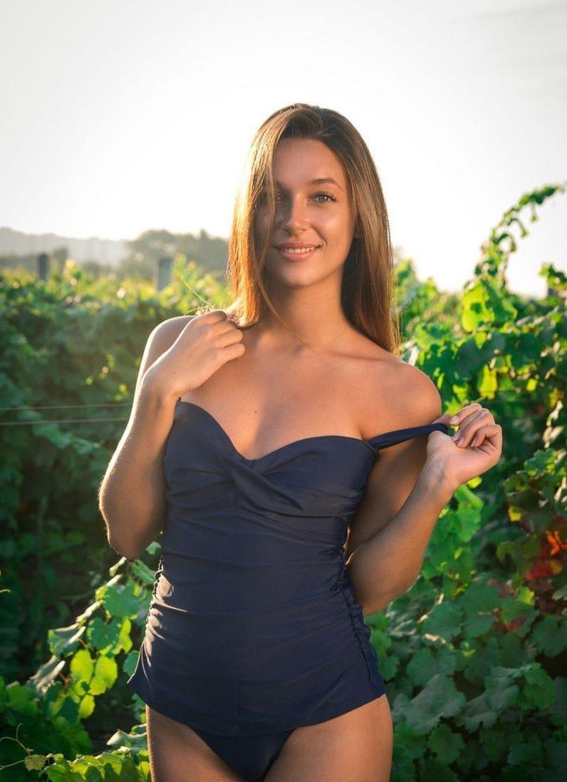 brunette girl reveals her black one-piece swimsuit outside in the nature