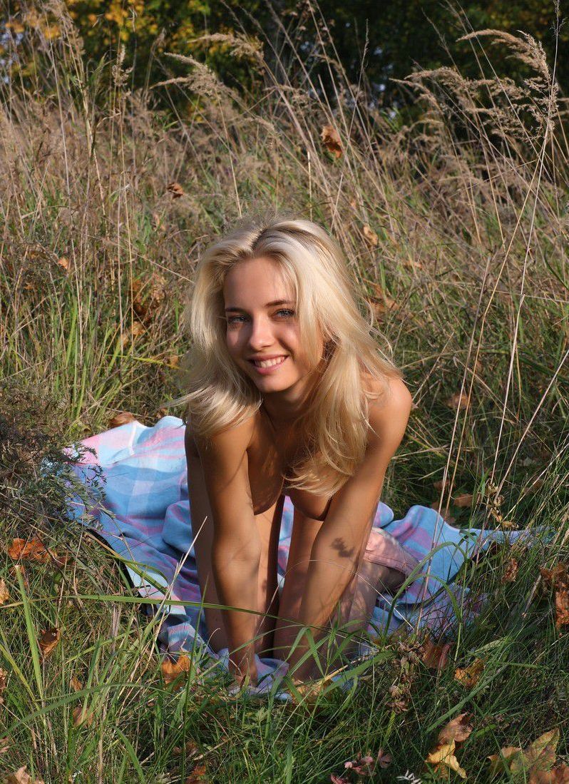 cute young blonde girl reveals her white gee string panties outside on the glade field in the nature