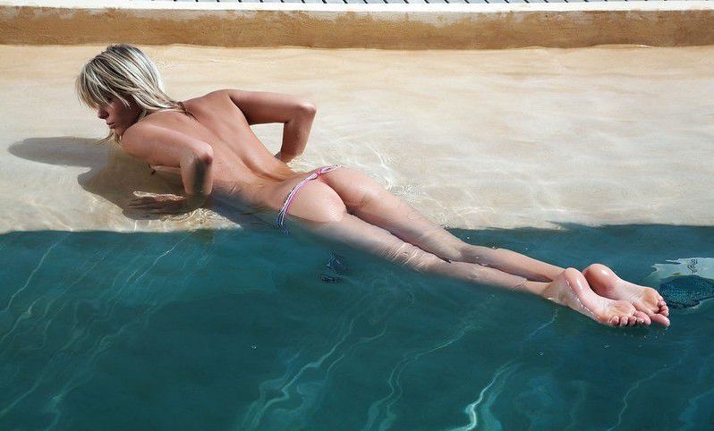 young blonde girl posing in the infinity edge pool at the sea