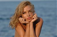 Babes: curly blonde girl with a blue top reveals on the rocky shore