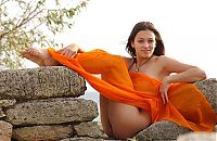 Babes: cute young brunette girl with full breasts and an orange scarf reveals near the wall of stones