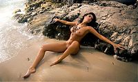 Babes: curly brunette girl reveals her body with necklaces at the sea on the rocky shore
