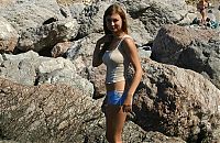 Babes: young brunette girl naturist undresses her sport undershirt and blue shorts in the sea on the public rocky beach