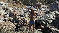 Babes: young brunette girl naturist undresses her sport undershirt and blue shorts in the sea on the public rocky beach