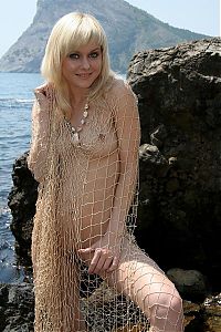 Babes: blonde girl reveals her shell necklace and fishing net on the rocky coast at the sea
