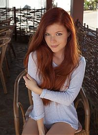 young red haired girl with facial freckles reveals her top and panties at the table with the rattan chair
